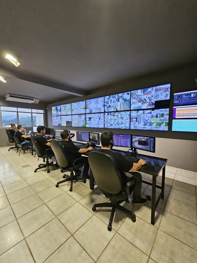 Vista da central de monitoramento com operadores nas estações e o videowall ao fundo